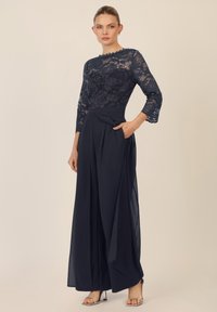 Conjunto de dos piezas en azul marino con una blusa de encaje transparente que presenta patrones florales y mangas de tres cuartos, combinada con pantalones anchos y fluidos.