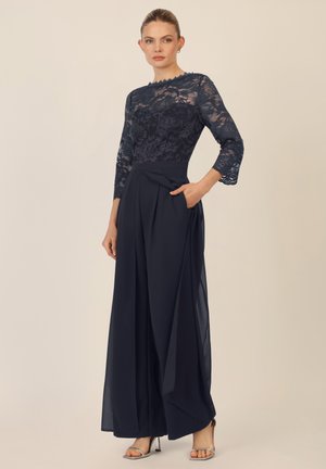 Navy blue kaksi-osainen asu, jossa on läpikuultava pitsitoppi kukkakuosisilla ja kolmanneksen pituisilla hihoilla, yhdistettynä löysiin leveisiin housuihin.