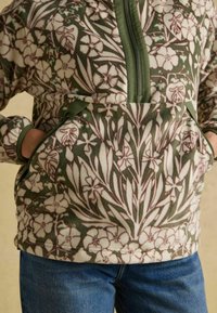 Fleecová mikina s květinovým vzorem v zelené a krémové barvě, se zipem na přední části a klokaní kapsou. Má jemnou texturu a kontrastní lemování.