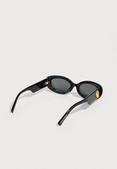 Μαύρα οβάλ γυαλιά ηλίου με σκοτεινούς φακούς, χρυσό έμβλημα λιονταριού στα πλαϊνά και λογότυπο "Dolce & Gabbana" σε ένα από τα μπράτσα.