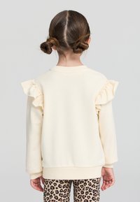 Felpa crema con dettagli a volant sulle spalle, polsini e orlo a coste, abbinata a leggings a stampa leopardata. Texture liscia, vestibilità casual.