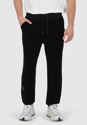 Schwarze Fleece-Jogginghosen mit einem Kordelzugbund, Seitentaschen und einem kleinen goldenen Logo am unteren Bein. Weicher Stoff, lässige Passform.