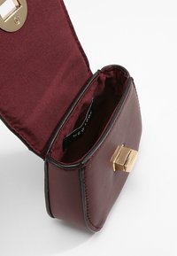 Sac en faux cuir bourgogne avec quincaillerie dorée, de forme rectangulaire, fermeture magnétique et intérieur doublé avec une étiquette de marque.