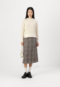 Maglione di crema con texture, orlo a costine, gonna midi a quadri nei toni del marrone, scarpe slip-on nere, calzini bianchi e una piccola borsa a tracolla color crema.