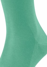 Calzino verde in cotone caratterizzato da una trama liscia e a costine, con punta senza cuciture e una vestibilità aderente. Il design è semplice e di un colore uniforme.