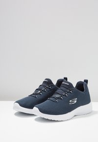 Scarpe da ginnastica blu navy con tomaia in rete, suola bianca, finitura testurizzata e lacci elastici. Presentano un logo sul lato e un tab sul tallone.