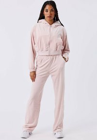 Roze velours trainingspak met een ritsjes-hoodie, elastische tailleband en lange mouwen. Opmerkelijke details zijn onder andere zijzakken en een ontspannen pasvorm.