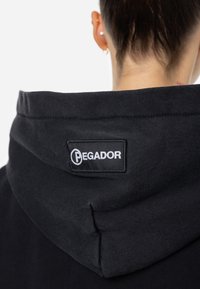 Čierna mikina s širokým golierom, na zadnej strane so šitým bielym logom "PEGADOR". Mäkkučká, textúrovaná látka.