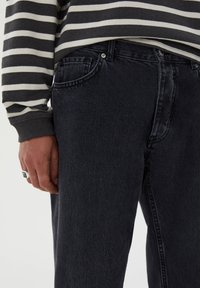 Jeans de mezclilla negra con un acabado texturizado y costuras visibles. Combinados con una camiseta de manga larga a rayas en gris y blanco.