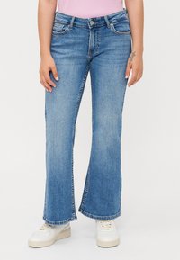 Lyseblå denim flared jeans med mid-rise midje, som har fem lommer og subtil fading, parret med hvite sneakers.