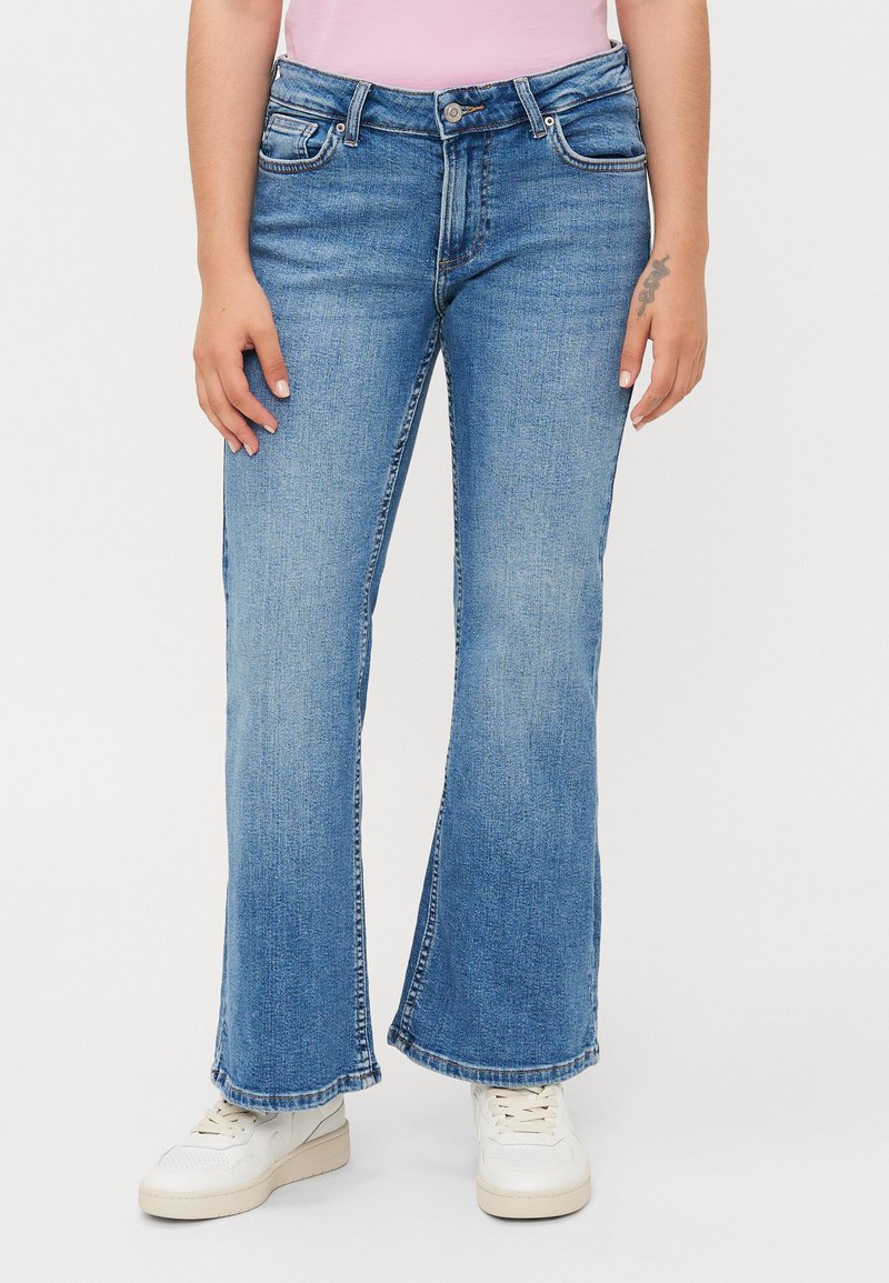 Lyseblå denim flared jeans med mid-rise midje, som har fem lommer og subtil fading, parret med hvite sneakers.