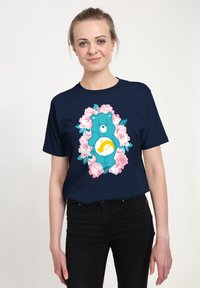 Marineblauw t-shirt met een afbeelding van een blauwe beer omringd door roze rozen en groene bladeren, met een gele maanvorm op de buik van de beer.