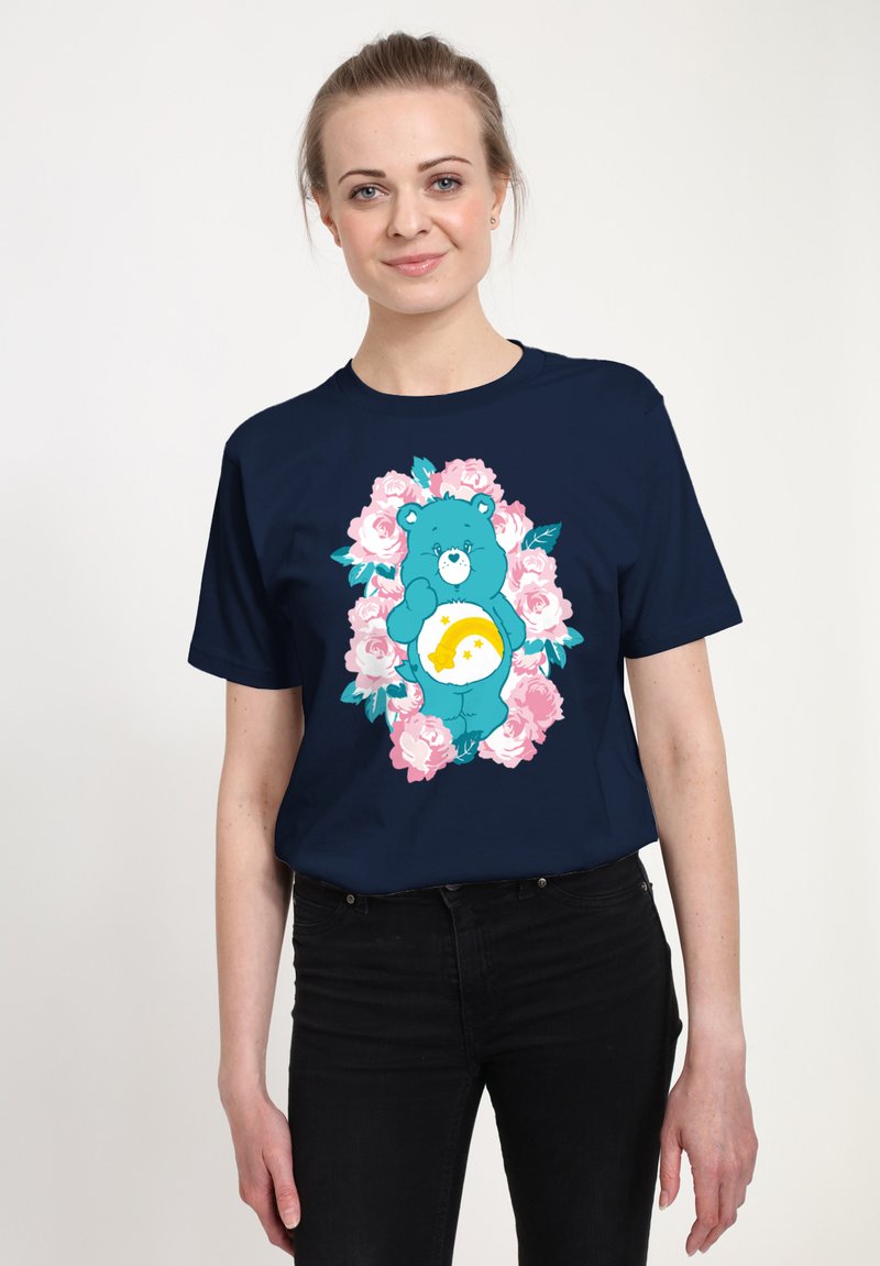 Marineblauw t-shirt met een afbeelding van een blauwe beer omringd door roze rozen en groene bladeren, met een gele maanvorm op de buik van de beer.