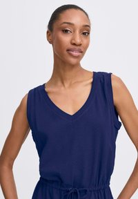 Navy blue sleeveless dress with a v-neckline and adjustable drawstring waist. Soft, textured fabric with a relaxed fit.