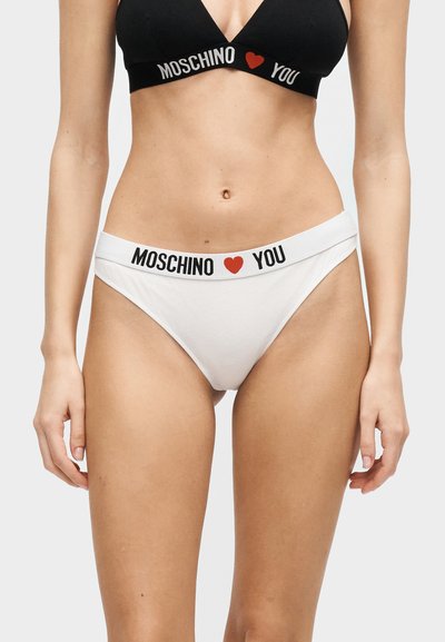 Γυναικείο σώμα που φοράει σετ εσωρούχων Moschino σε μαύρο και λευκό με κόκκινη καρδιά ανάμεσα στα κείμενα "Moschino" και "You".