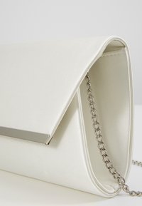 Bílá saténová kabelka na ruku se stříbrnou sponou, vybavená řetízkovým popruhem. Design je elegantní s hladkým povrchem a trojúhelníkovou klopou.