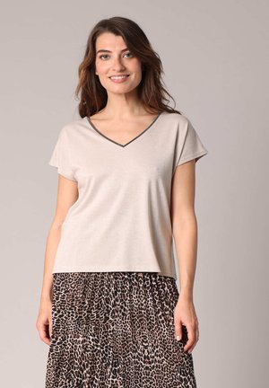 Haut beige clair à manches courtes avec un décolleté en V, présentant un léger éclat et une bordure noire le long du col. Texture lisse, coupe décontractée.