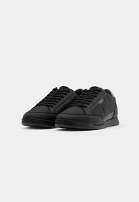 Black athletic shoes made of smooth synthetic material featuring a low-top design, padded collar, textured accents, and flat laces.