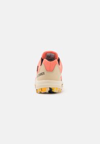 Zapatilla de trail ligera con parte superior de malla rosa, soporte en el talón beige y suela de goma con un estampado colorido para una mayor tracción.