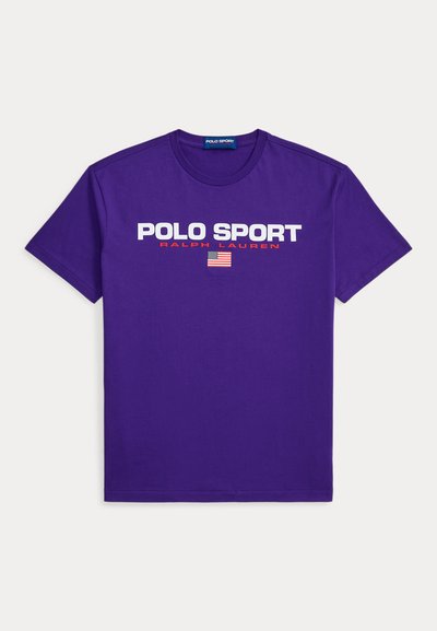 T-shirt en coton violet arborant les inscriptions "POLO SPORT" et "RALPH LAUREN" en texte blanc et rouge, avec un motif de drapeau américain centré en dessous.