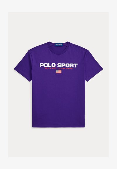 T-shirt en coton violet arborant les inscriptions "POLO SPORT" et "RALPH LAUREN" en texte blanc et rouge, avec un motif de drapeau américain centré en dessous.