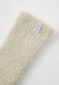 Calzino beige morbido con una superficie testurizzata e un'etichetta tessuta che presenta la parola "BOSS" in argento. Il design è accogliente e caldo.