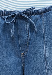 Μπλε τζιν παντελόνι με ελαστική μέση και δέσιμο με κορδόνι, φορεμένο με ριγέ μπλε και λευκή μπλούζα.