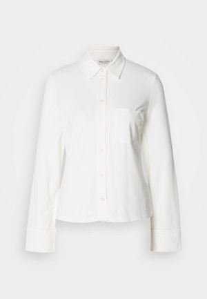 Camicia bianca a maniche lunghe con collo a punta, taschino sul petto anteriore e maniche con polsini, esposta su uno sfondo semplice.