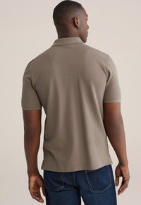 Korte mouwen, polo met kraag in olijfgroen, gemaakt van zachte stof. De achteraanzicht toont een rechte zoom en zijsplitten voor extra comfort.