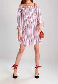 Olkapäiltä oleva mekko punaisilla ja sinisillä pystysuorilla raidoilla, kolmivartiset hihat sitomalla, rento malli, yhdistetty mustiin korkokenkiin ja punaisiin nilkkasiteisiin.