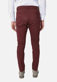 Pantaloni bordeaux in cotone con vestibilità slim, dotati di due tasche posteriori e un piccolo etichetta con logo in vita, abbinati a stivaletti grigi alla caviglia.