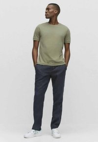 Olivgrön t-shirt med kort ärm, mörkblå byxor och vita sneakers med gröna detaljer. Avslappnad passform och enkel design.
