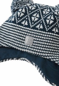 Dziany zimowy czapka w ciemnoniebieskim i białym kolorze z geometrycznym wzorem, z dwiema pomponami na górze oraz szarym logo z boku.