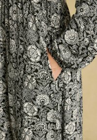 Schwarz-weiß gemustertes Kleid mit Blumenmuster aus leichtem Stoff, mit gerafftem Oberteil, langen Ärmeln und seitlicher Taschenapplikation.