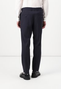 Pantalones ajustados azul marino con una textura suave, que cuentan con dos bolsillos traseros y cierres de botón negro. Combinados con una camisa de color claro y zapatos.