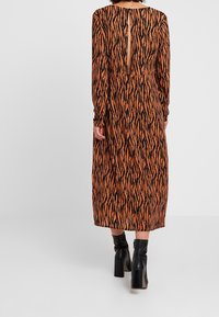 Donna in un abito midi a maniche lunghe con stampa zebra arancione e nera, caratterizzato da uno spacco posteriore, abbinato a stivaletti neri con tacco.