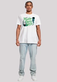 Camiseta blanca de algodón con un diseño gráfico colorido que presenta el texto "Maestro de las Artes Oscuras", con personajes y formas de estilo caricaturesco.