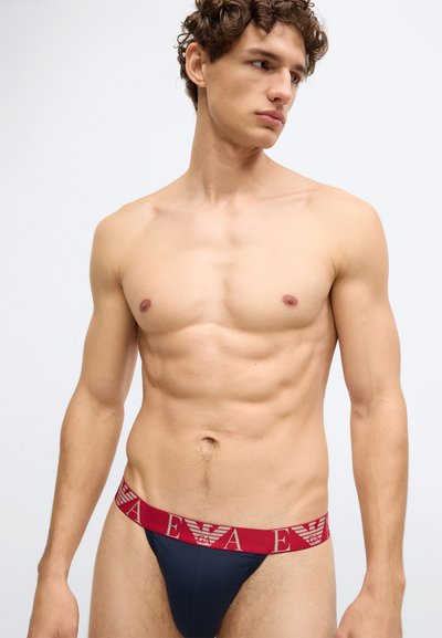 Tanga azul-marinho com uma cintura elástica vermelha com um logótipo. O design é minimalista com uma textura de tecido lisa.