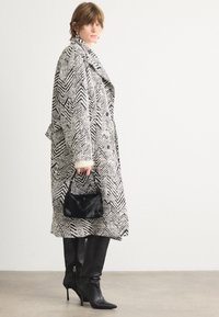 Abrigo de cuadros en blanco y negro con cuello ancho, estilo de doble botonadura, combinado con elegantes botas de tacón negro y un pequeño bolso negro.