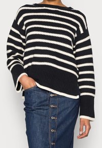 Svartvit randig stickad tröja med ribbat mönster, vida ärmar och rundad nederkant, kombinerad med enjeanskjol med knappdetaljer.