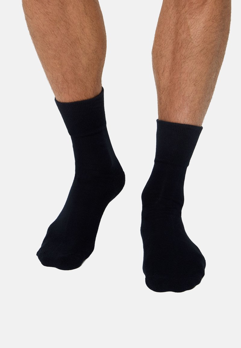 Sorte bomuldssokker med ribbet kant, sømløs konstruktion og en glat tekstur. Placeret på bare fødder mod en neutral baggrund.