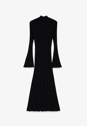 Dolga črna pletena obleka z visokim ovratnikom in razširjenimi rokavi v obliku zvona, oprijeta okoli trupa in bokov, razširjena do širokega roba.