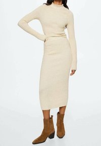 Úpletový dvoudílný set v světlé krémové barvě, obsahující top s dlouhým rukávem a tužkovou sukni. Texturovaná tkanina s přiléhavým střihem. Hnědé kotníkové boty na podpatku.