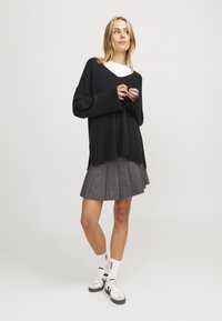 Černý oversize pletený svetr, šedá skládací sukně, bílé ponožky s černými akcenty a šedé tenisky. Hladká textura a uvolněný střih.