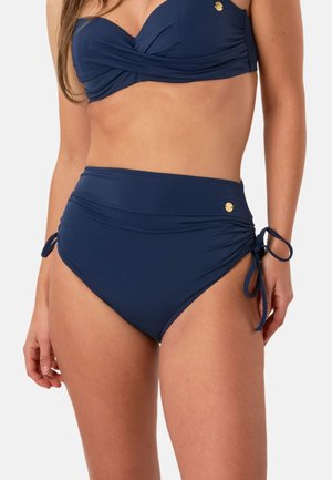 Femme portant un maillot de bain deux-pièces bleu marine avec un bas taille haute avec des liens sur les côtés et un design torsadé sur le haut.