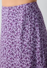 Gonna floreale in lavanda con vita aderente e zip laterale. Presenta un motivo di piccoli fiori viola su un tessuto testurizzato.