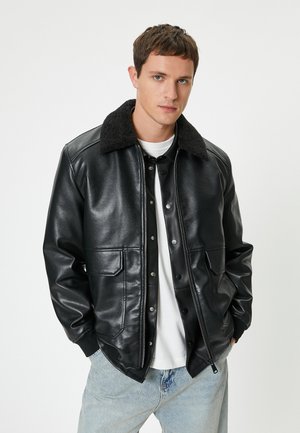 Chaqueta de cuero negra con un cuello texturizado negro, botones a presión, dos bolsillos delanteros y un diseño ajustado, combinada con jeans azul claro.