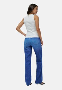 Weißes, geripptes, ärmelloses Top mit einem Schlüssel-Loch Rücken, kombiniert mit blauen, hochtaillierten, ausgestellten Jeans mit Gesäßtaschen und einer lockeren Passform.