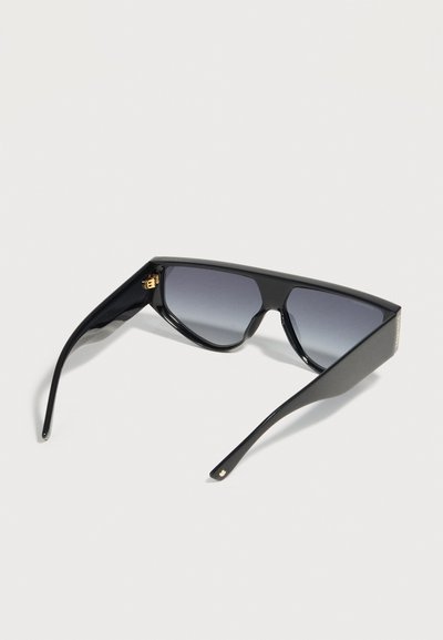 Μαύρα υπερμέγεθη ορθογώνια γυαλιά ηλίου με βαθμιαία σκουρόχρωμους φακούς και χοντρές πλευρικές βάσεις, ανοιχτά τοποθετημένα σε ανοιχτογκρι επιφάνεια.