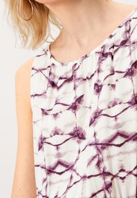 Ärmelloses Oberteil mit weißem Grund, das ein lila abstraktes Muster, einen gefalteten Ausschnitt und eine glatte Textur aufweist. Leichter Stoff.